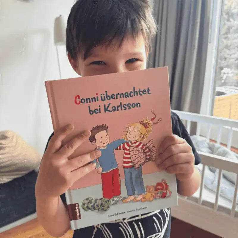 dunkelhaariger Junge schaut hinter seine personalisierten Conni-Buch hervor.