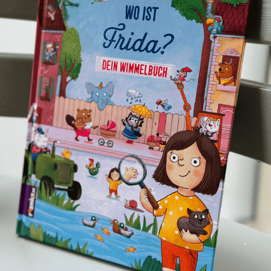 Kinderbuch mit dem Titel "Wo ist Frida?" - Dein Wimmelbuch zeigt ein Mädchen, das eine Katze und eine Lupe in der Hand hält mit lebhaften tierischen und menschlichen Figuren in einer farbenfrohen Szene im Freien.