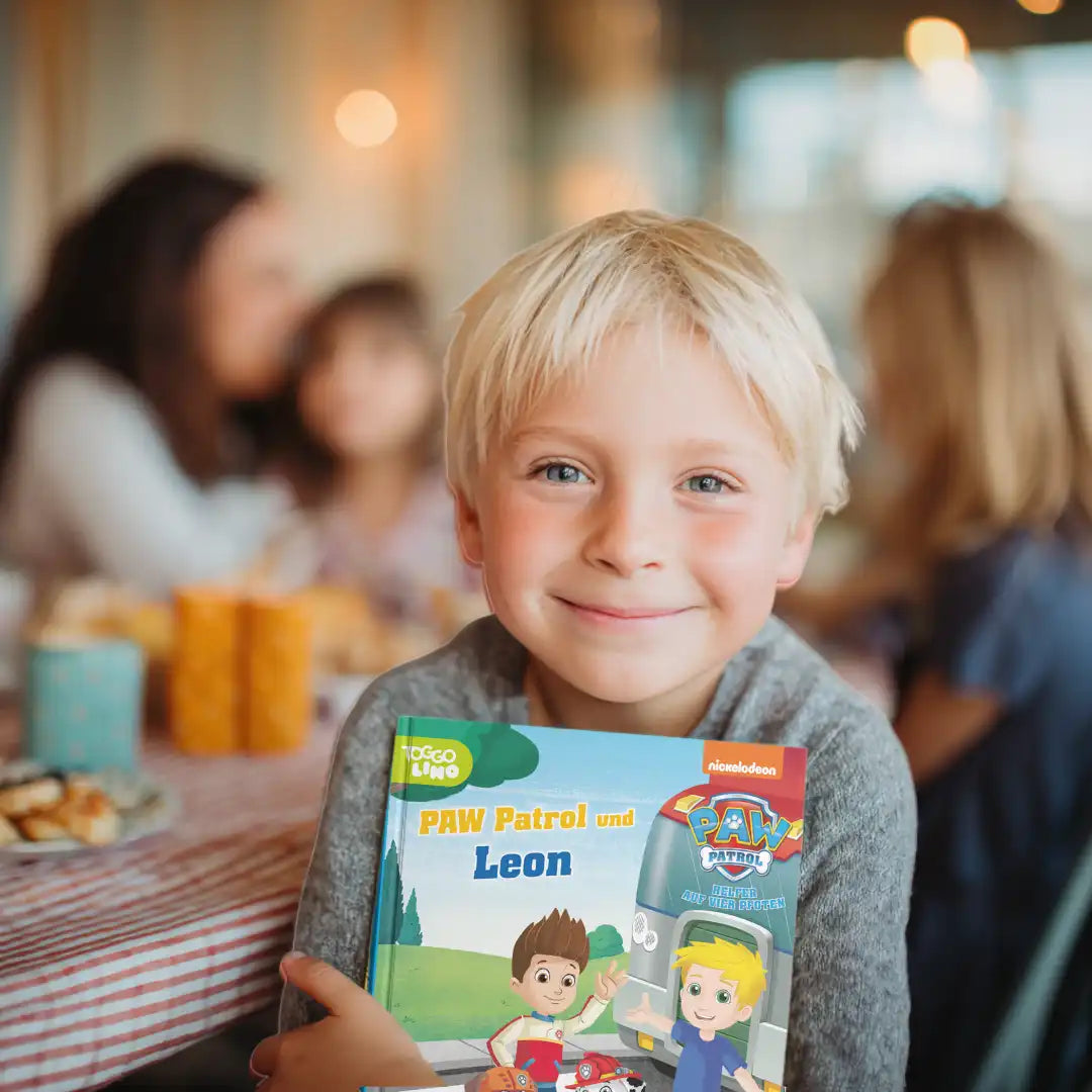 Blonder Junge hält freudig strahlend das personalisierte Buch "Paw Patrol und Leon" im Arm