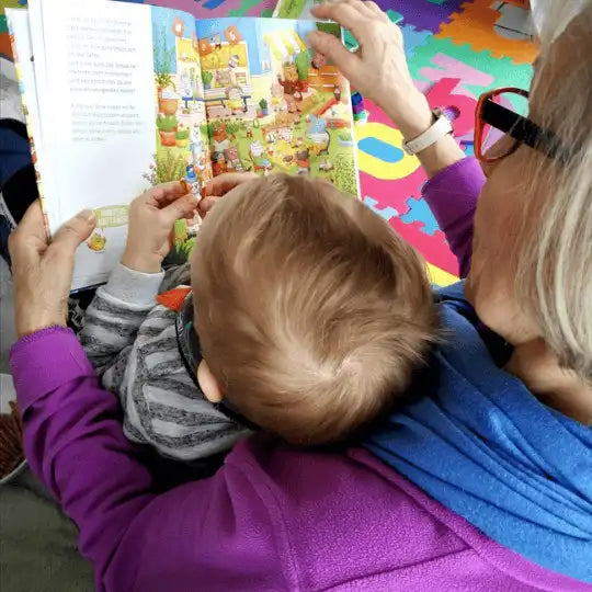 Kind und Oma sitzen auf dem Boden und schauen sich gemeinsam ein Wimmelbuch an